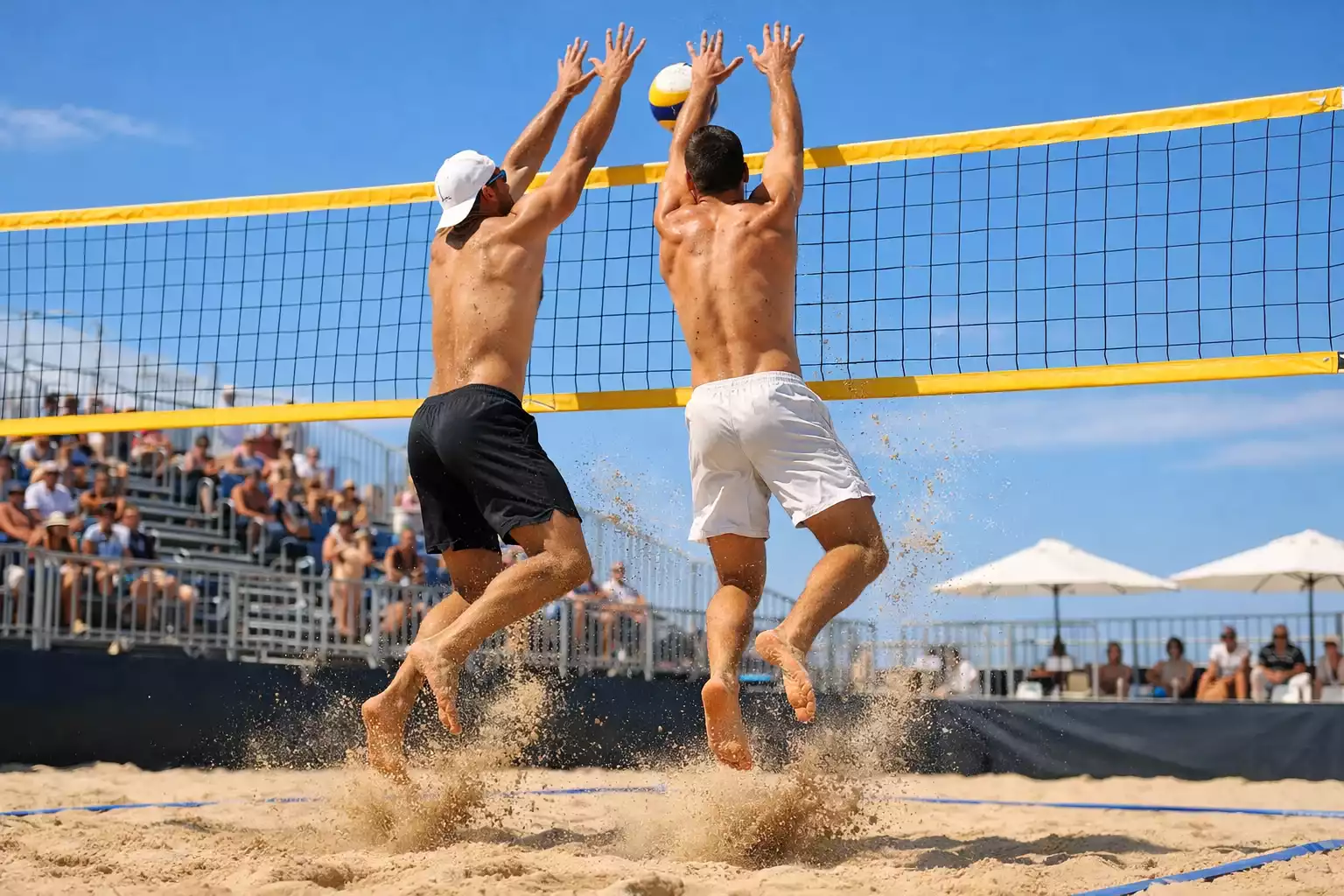 Beachvolleyball-Duo beim Sprung am Netz auf einem Sandplatz bei Sonnenschein